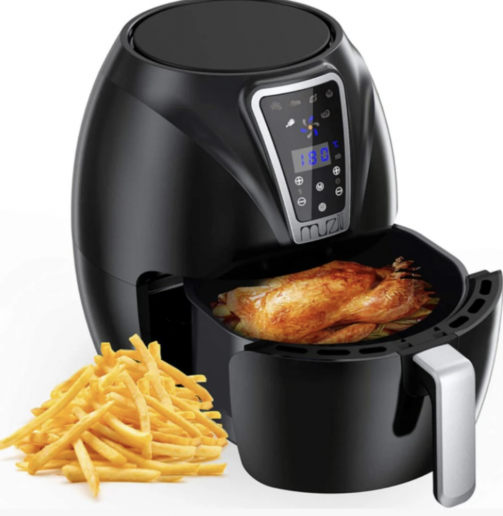 A black air fryer with a digital control panel displaying a temperature of 180°C. The fryer basket is pulled out, revealing a whole roasted chicken inside. Next to the air fryer, there is a heap of cooked French fries.