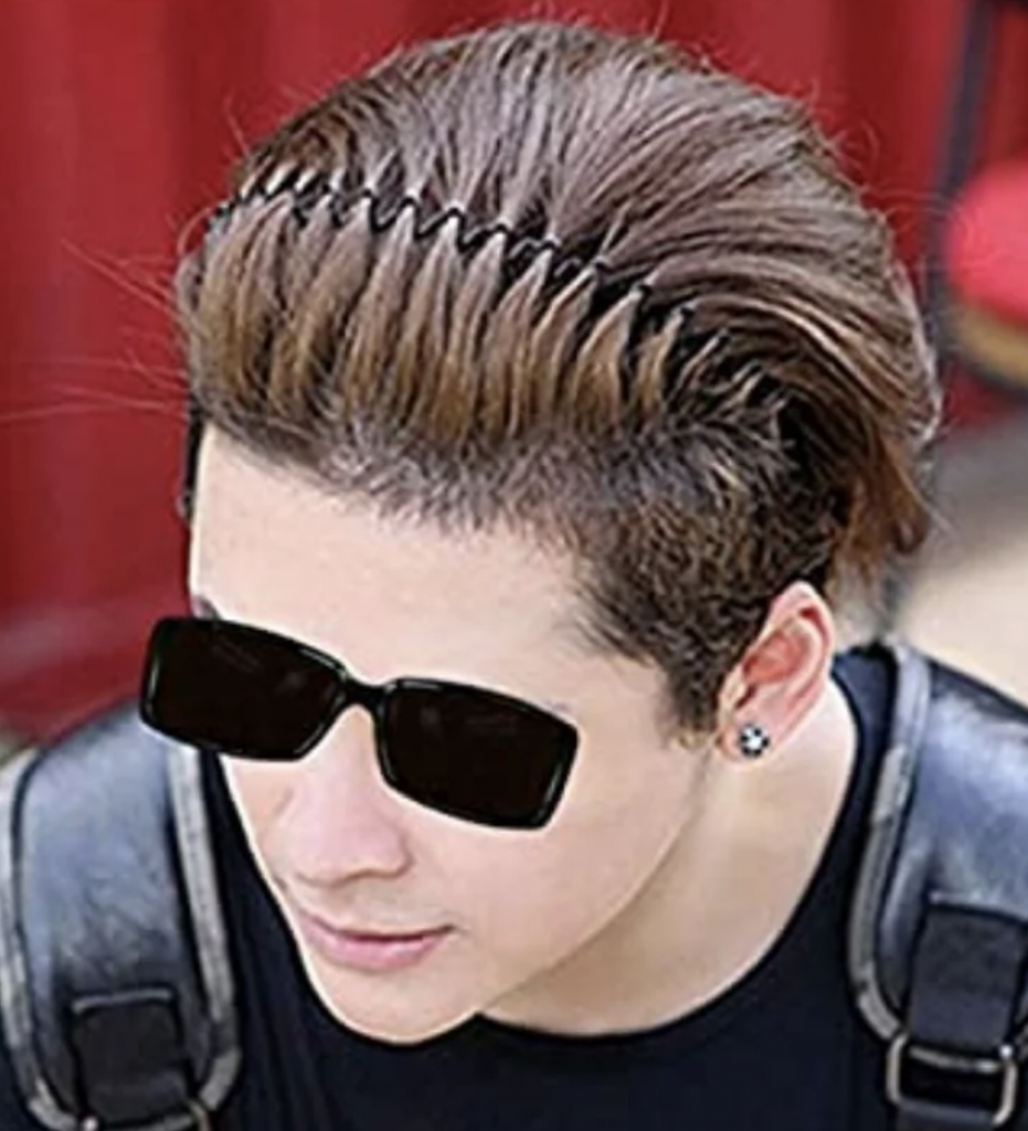 Person with short brown hair held back by a hairband, wearing black sunglasses, a black shirt, and a black leather backpack, sitting against a red background.