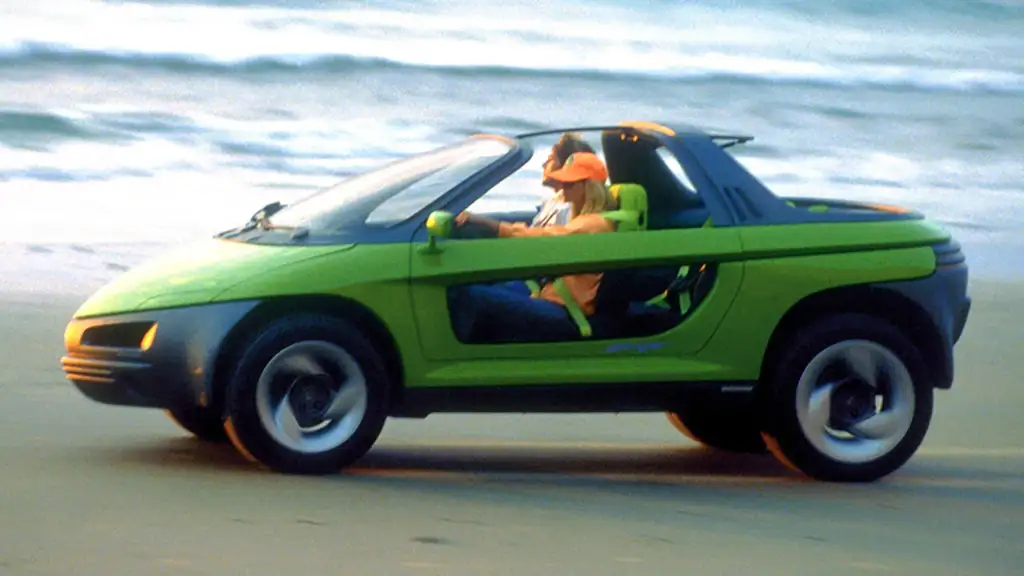 A vibrant green, compact, convertible car with an open top is being driven on a beach. Two occupants are in the vehicle, the driver wearing a cap. The ocean and waves are slightly blurred in the background, enhancing the sense of motion.