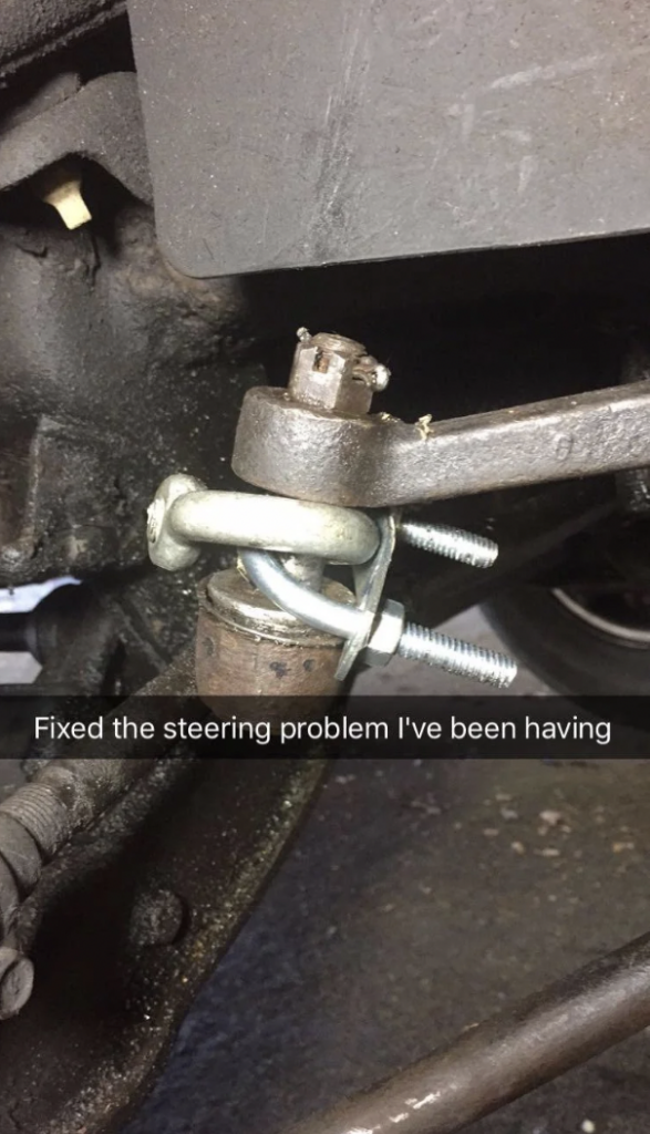 Close-up of a car’s steering mechanism, showing a crude, temporary fix. A U-bolt and two nuts secure a broken or disconnected part, with visible grime and wear on the surrounding metal surfaces. The text overlay reads, "Fixed the steering problem I've been having.