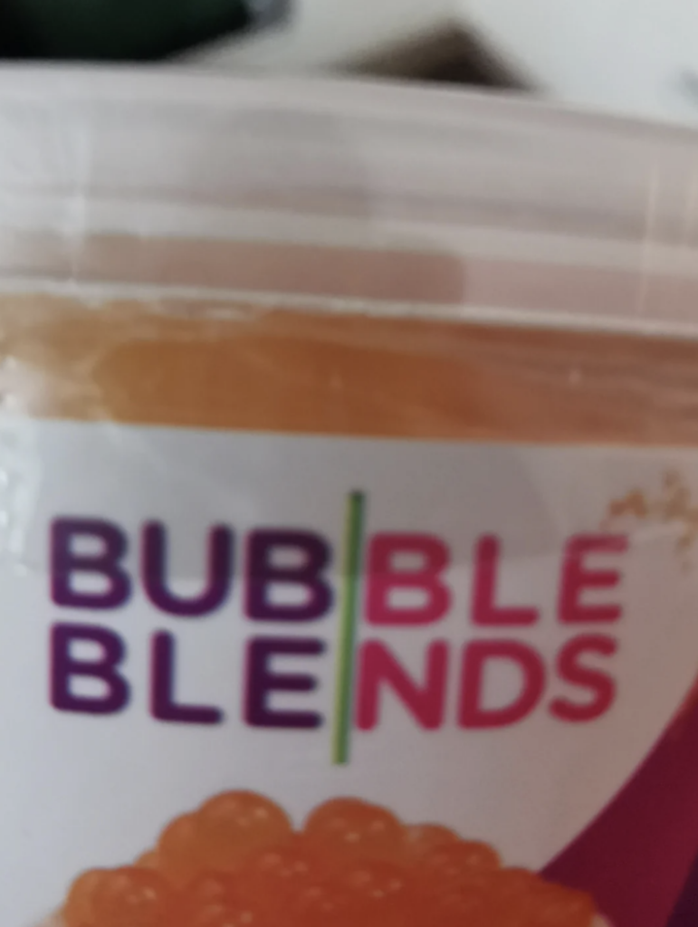 A close-up photo of a product label showing the brand name "Bubble Blends" in bold, colorful letters. The top part of the container is visible with a translucent lid showing an orange substance inside.
