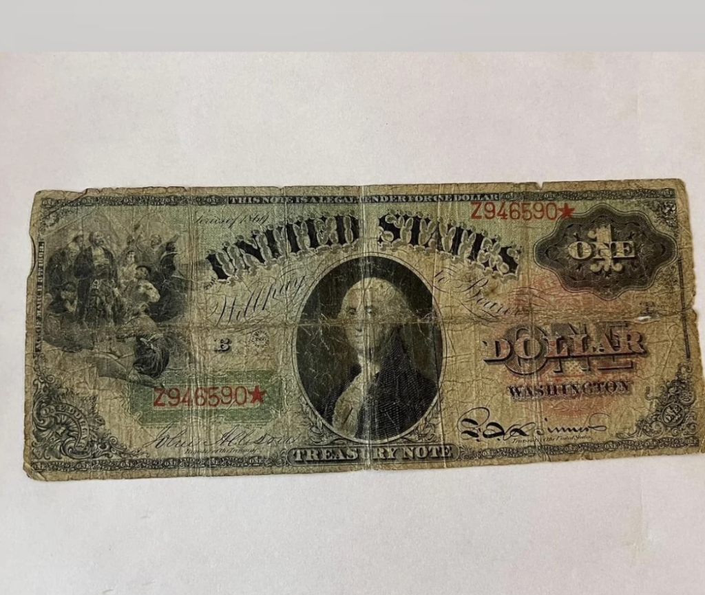 A worn vintage one dollar bill featuring a portrait of George Washington in the center. The bill has text saying "United States" and "One Dollar" and is marked with red serial numbers "2946590" in the corners. The edges appear frayed and tattered.