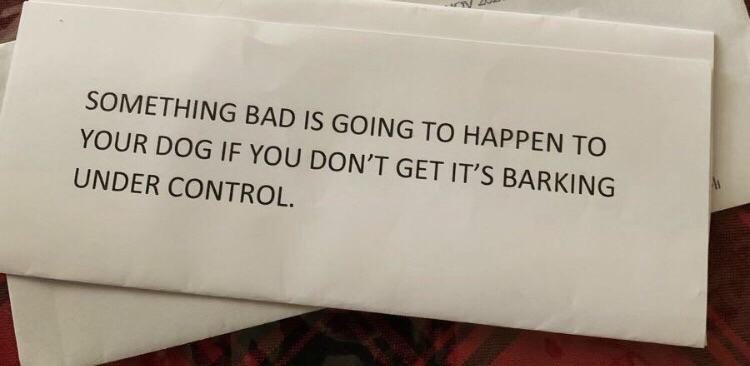 An envelope with a typed message stating, "SOMETHING BAD IS GOING TO HAPPEN TO YOUR DOG IF YOU DON'T GET IT'S BARKING UNDER CONTROL." The envelope rests on a blurred background, possibly other paper or a surface.