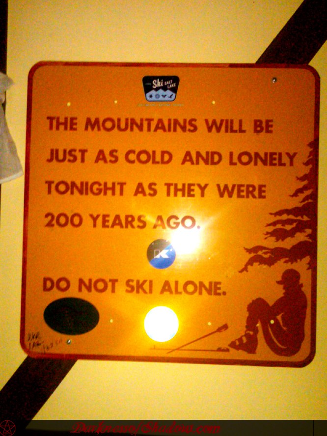 An orange sign reads, "The mountains will be just as cold and lonely tonight as they were 200 years ago. Do not ski alone." The background features an illustration of a skier sitting on a slope with trees in the distance.