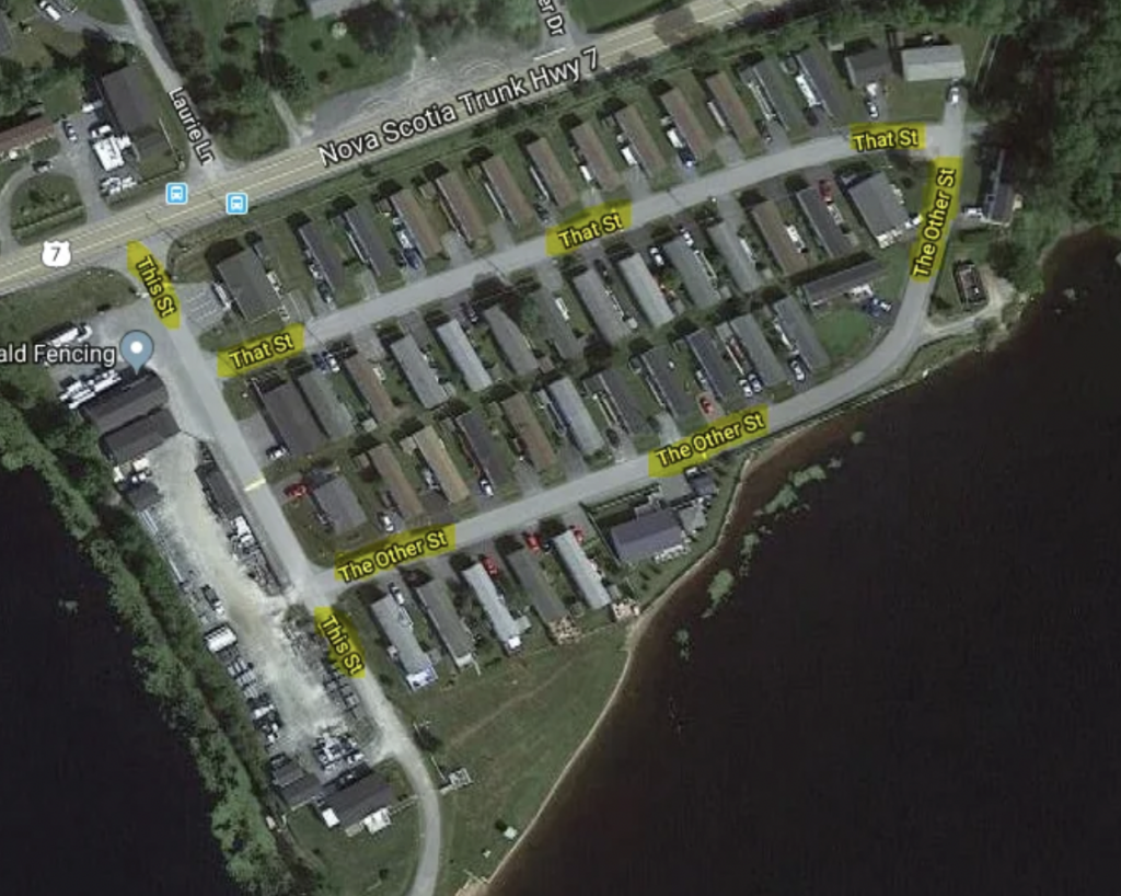 A satellite image shows a small neighborhood near a lake and Nova Scotia Trunk Hwy 7 labeled with humorous street names: "This St," "That St," "The Other St," and "The Other St" again. The area consists of several houses, with a fenced area near the highway.