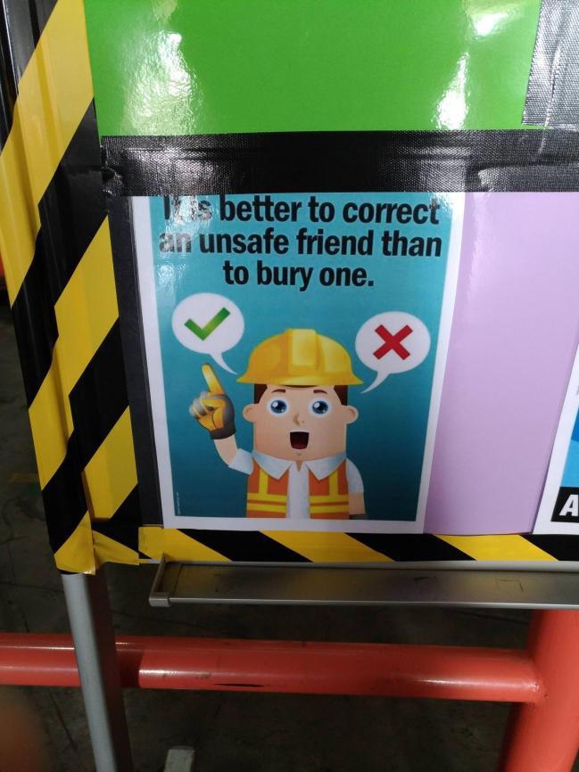 A workplace safety sign showing a cartoon construction worker wearing a hard hat and safety vest. The text reads, "It's better to correct an unsafe friend than to bury one." The worker is giving a thumbs up with a green check mark and a thumbs down with a red X.