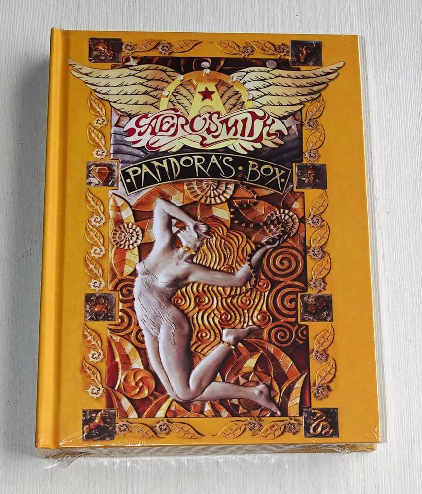 The image shows a hardcover book with a bright orange cover titled "Pandora's Box" by Aerosmith. The center features an intricate, classical-style illustration of a partially nude figure, surrounded by ornate patterns and an angelic figure at the top.