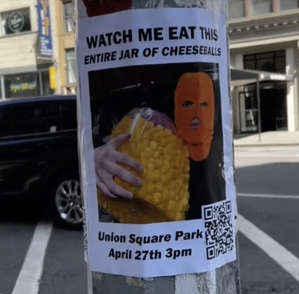 A poster on a pole features a masked person holding a large jar of cheeseballs. The text reads, "WATCH ME EAT THIS ENTIRE JAR OF CHEESEBALLS" with details "Union Square Park April 27th 3pm" and a QR code at the bottom right.