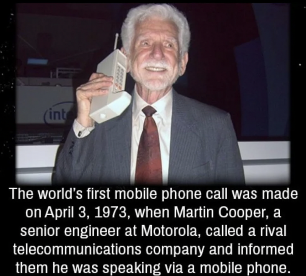 An elderly man in a suit and tie holds a large, early-model mobile phone to his ear while smiling. The accompanying text mentions that Martin Cooper, a senior engineer at Motorola, made the world's first mobile phone call on April 3, 1973.