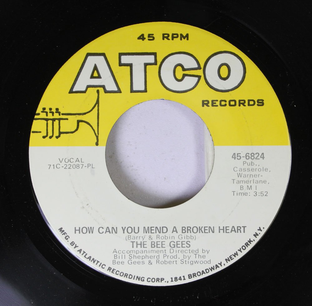 A close-up of a vinyl record with a yellow and white ATCO Records label. The song title "How Can You Mend a Broken Heart" by The Bee Gees is prominently displayed. Additional text includes production credits and track information. The record is set at 45 RPM.