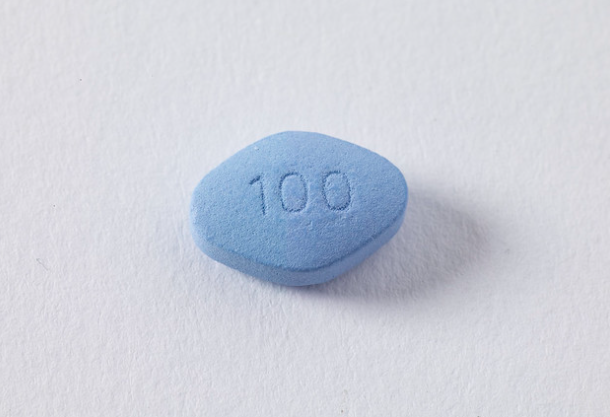 A close-up of a single blue, diamond-shaped pill with the number "100" embossed on one side, positioned on a plain white background.