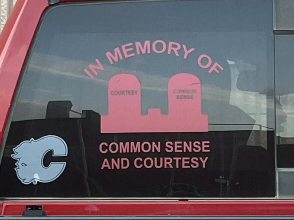 A car window decal features two tombstones labeled "COURTESY" and "COMMON SENSE" with the words "IN MEMORY OF COMMON SENSE AND COURTESY" written above and below them in pink letters. A cartoon sheep icon with the letter "C" is also present.