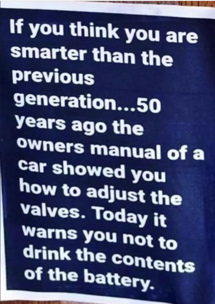 A sign with white text on a dark blue background reads: "If you think you are smarter than the previous generation... 50 years ago the owners manual of a car showed you how to adjust the valves. Today it warns you not to drink the contents of the battery.