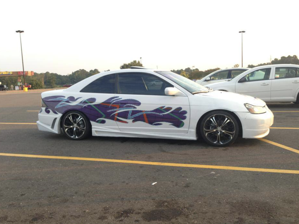 A white car with custom purple and green graffiti-style artwork on its side is parked in a lot. The car has dark tinted windows and large black alloy wheels. Other vehicles and a landscape with trees are visible in the background.