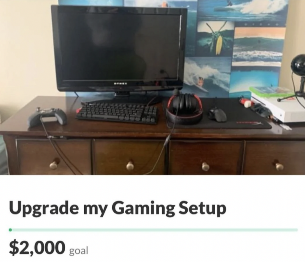 A wooden desk holds a computer monitor, gaming controller, keyboard, headphones, and mouse pad. Behind, a wall features a collage of surfing images. Text at the bottom reads, "Upgrade my Gaming Setup" with a fundraising goal of $2,000.