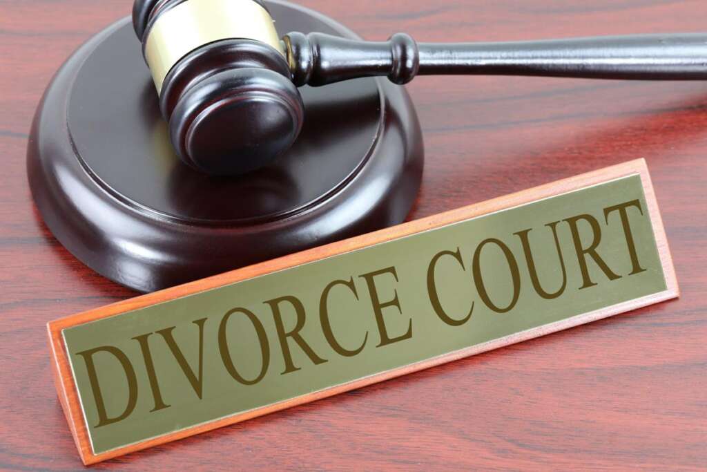 A wooden gavel rests on its sounding block next to a sign that reads "DIVORCE COURT" on a wooden surface.