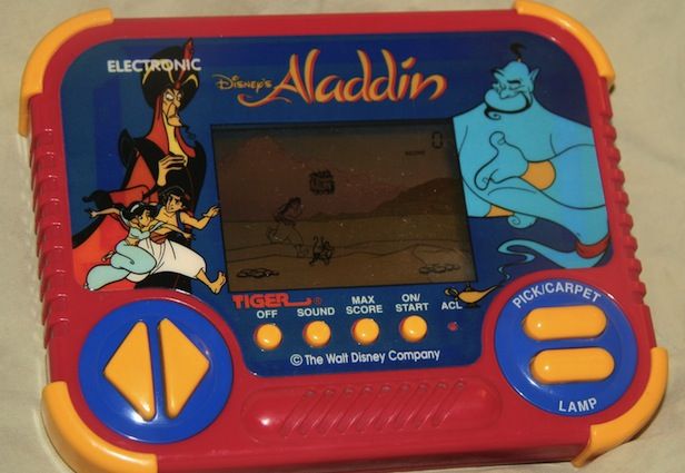 A vintage Disney Aladdin handheld electronic game by Tiger Electronics is displayed. The game features Aladdin and Genie illustrations on the red and blue casing. The screen shows gameplay, and the control buttons are yellow and blue. "Disney's Aladdin" is written on top.