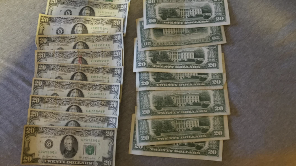 A collection of U.S. paper currency is arranged on a surface. On the left, there are fifteen $2 bills featuring Thomas Jefferson. On the right, there are twelve $20 bills with a mix of front and back sides showing Andrew Jackson and the White House.