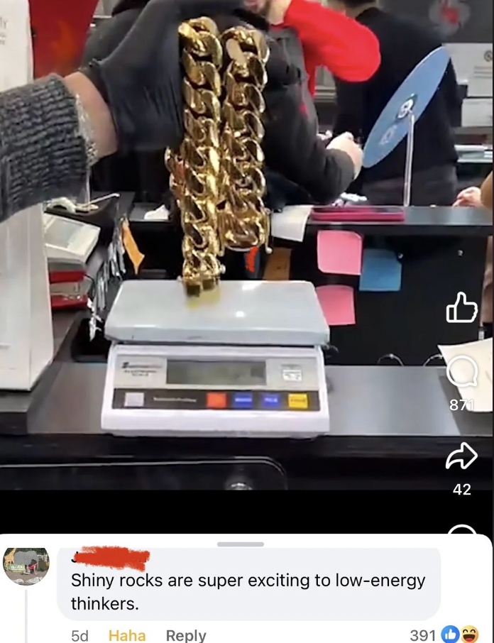 A gold chain is being weighed on a digital scale at a counter. Someone wearing a gray sleeve holds the chain. The setting appears to be a store with employees in the background. A comment below the image reads, "Shiny rocks are super exciting to low-energy thinkers.