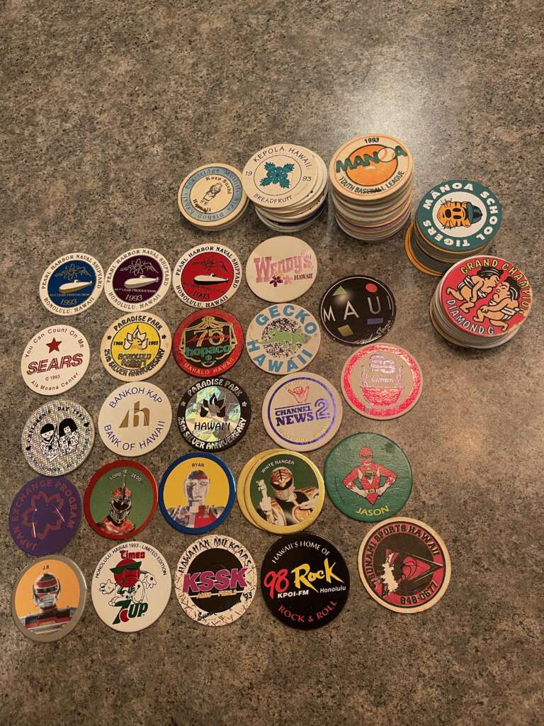 A collection of various colorful wooden tokens laid out on a speckled countertop. They feature designs from different establishments, events, and characters, including restaurants, radio stations, and promotional tokens. Several stacks of tokens appear on the right side.