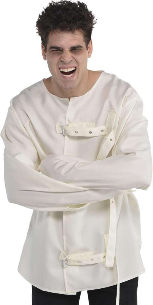 A person with dark hair is wearing a white straitjacket, with their arms crossed and secured. The person has a facial expression that appears to be either angry or in pain. The background is plain white, and the person is wearing dark pants.