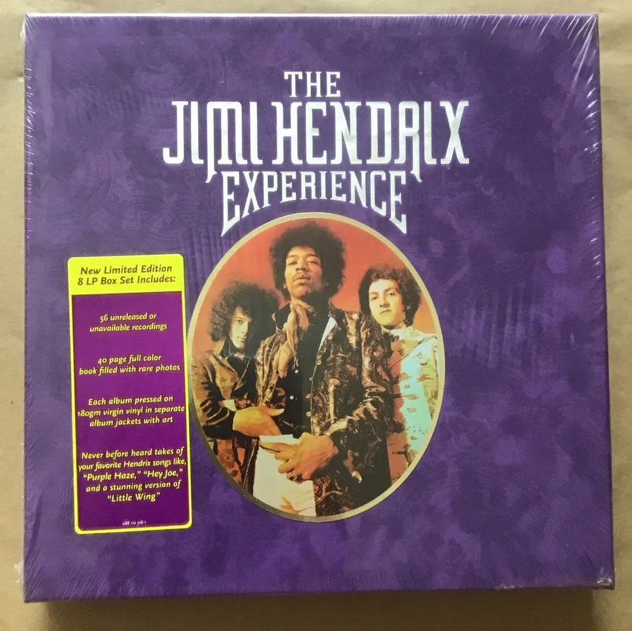 Box set cover of "The Jimi Hendrix Experience", featuring a purple background with text and a central oval image of three band members. A yellow sticker on the left lists contents, including 8 LPs, a 36-page booklet, and detailed information about the albums.