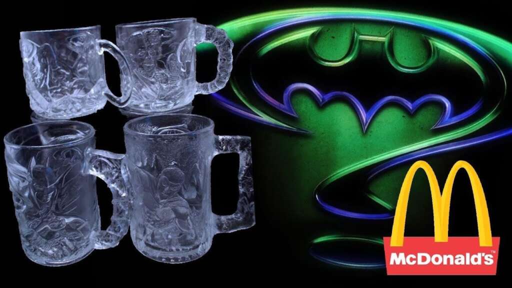 The image shows four intricately designed glass mugs with Batman artwork on the left side. On the right side, there is a glowing green and blue Batman logo accompanied by the McDonald's logo in the bottom right corner.