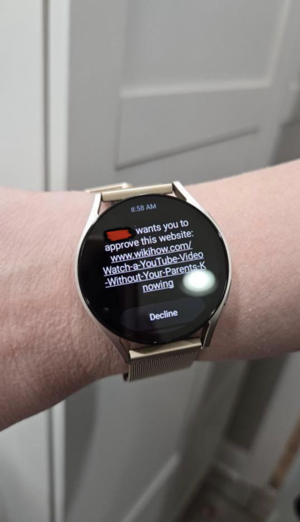 A person's wrist wearing a smartwatch with a notification displayed. The message reads, "wants you to approve this website: www.wikihow.com/Watch-a-YouTube-Video-Without-Your-Parents-Knowing." There is an option to decline the request. The time reads 8:58 AM.