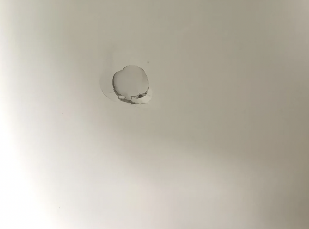 A white wall with a round hole in the center. The surrounding area shows signs of cracking and damage, indicating the wall has been impacted, creating the hole.