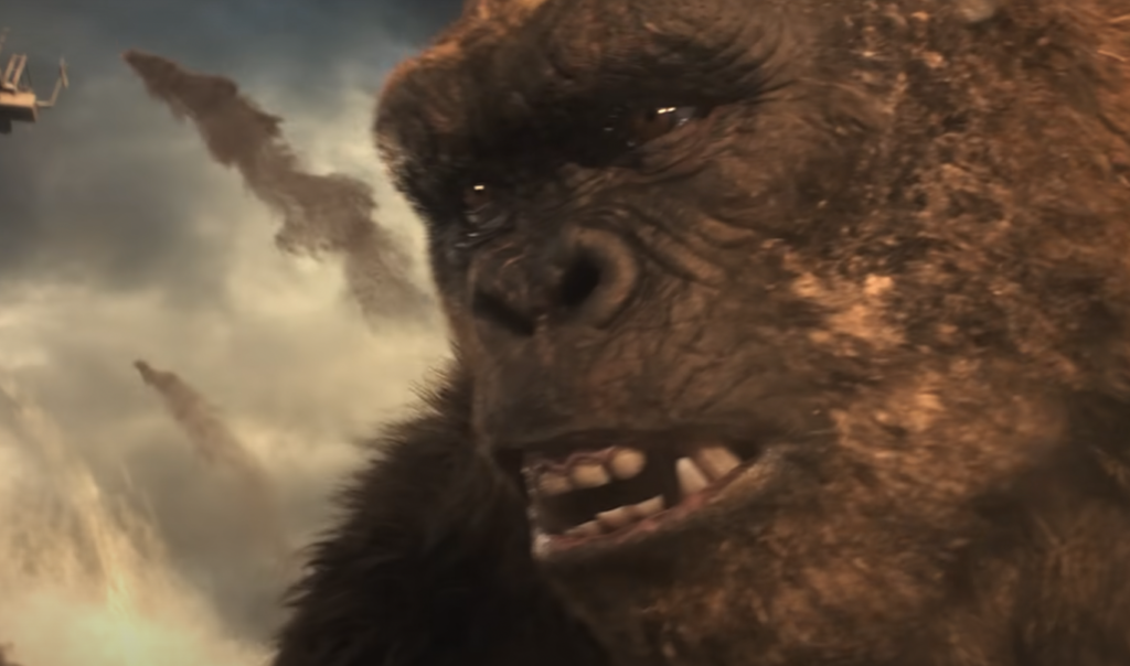 A close-up of a large, roaring gorilla-like creature with an expressive face, showing sharp teeth. The background features a chaotic scene with explosions and debris.