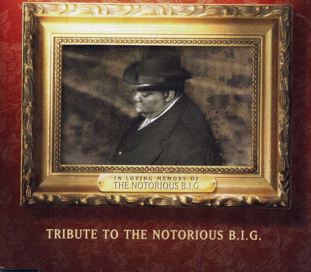 A framed photograph of a man dressed in a suit and hat is displayed against a red background. The frame features a plaque reading "In Loving Memory of The Notorious B.I.G." Below the frame, text reads "TRIBUTE TO THE NOTORIOUS B.I.G.