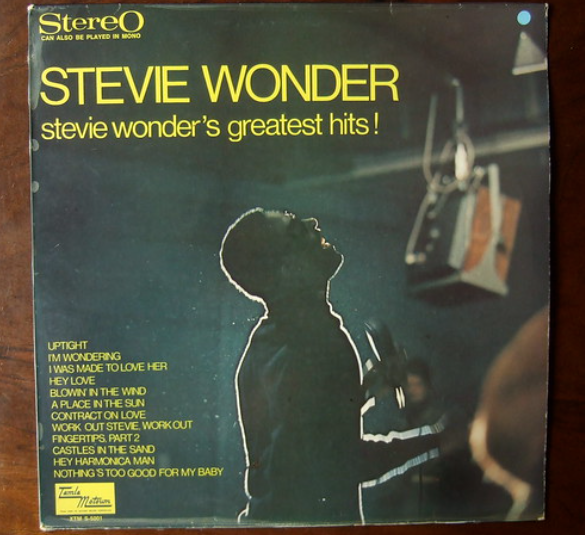 Album cover of "Stevie Wonder's Greatest Hits" by Stevie Wonder. The image features a silhouette of Stevie Wonder singing into a microphone. The album contains popular tracks such as "Uptight," "Hey Love," and "A Place in the Sun." The cover has a dark background.