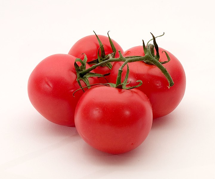 Four ripe, red tomatoes are clustered together on a vine. The tomatoes have smooth skins and are set against a plain white background, emphasizing their vibrant color. The green stems and leaves are still attached, adding a fresh look.