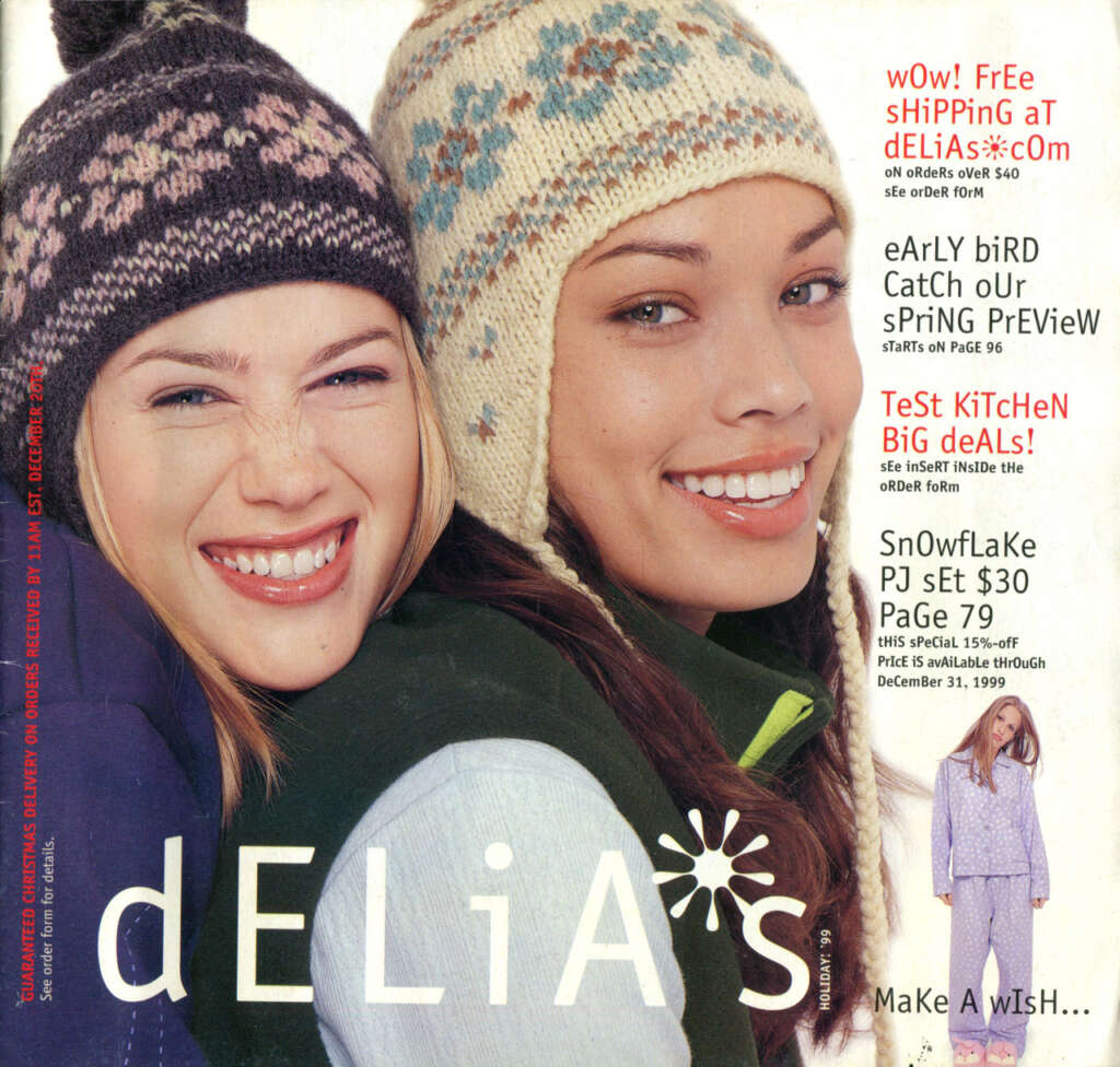 Two women smile warmly, wearing winter hats and cozy attire. The background displays various promotional text for dELiA*s, featuring offers like free shipping, early bird previews, gift ideas, and discounts. The magazine style layout presents a festive, cheerful vibe.