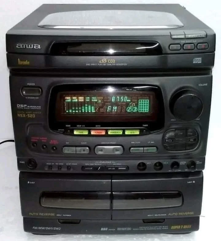 A vintage Aiwa stereo system featuring a multi-CD player on top, a digital display with equalizer visuals in the center, various control buttons and knobs below, a dual cassette deck at the bottom, and a pair of speakers on either side.
