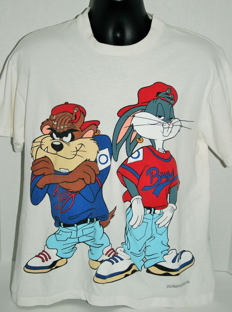 A white t-shirt featuring animated characters wearing baggy clothes and baseball caps. On the left is a character resembling an anthropomorphic Tasmanian Devil, and on the right is a character resembling an anthropomorphic rabbit with a red shirt and blue jeans.