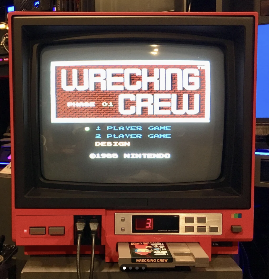 A vintage red-and-black television displays the title screen of the game "Wrecking Crew" by Nintendo. The screen offers options for "1 Player Game" and "2 Player Game Design." A game cartridge is inserted into the TV, and the number 3 is displayed below the screen.