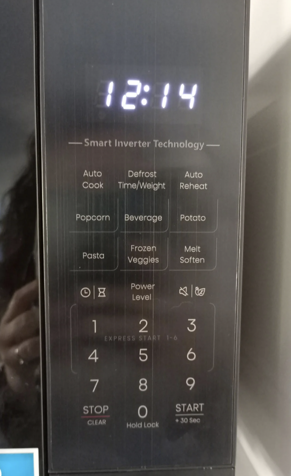 Close-up of a microwave oven control panel displaying 12:14. The panel includes functions such as Auto Cook, Defrost Time/Weight, Auto Reheat, Popcorn, Beverage, Baked Potato, Pizza, Frozen Veggies, Pasta, Melt Soften, and numeric keypad along with Start and Stop buttons.