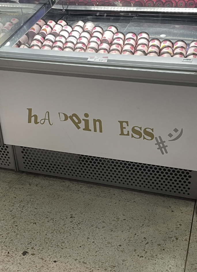 A refrigerated display case containing rows of packaged frozen desserts. The front of the display has a decorative sign with the stylized word "happiness" where some letters are replaced by symbols, making it hard to read at first glance.