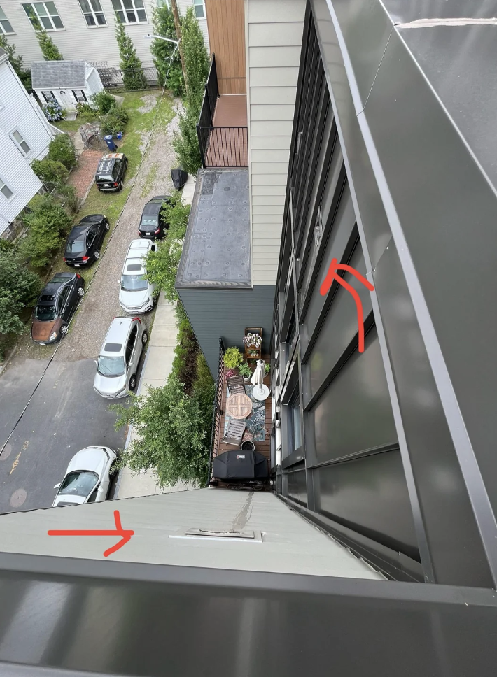 View from a rooftop looking down at some cars parked along a street and a small outdoor patio area between two narrow buildings. Red arrows are drawn on the image, pointing to various spots on the buildings.