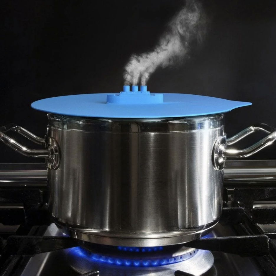 A metal pot with a blue silicone lid, shaped like a ship, is on a stovetop with a blue flame underneath. Steam is coming out of a small ship-like structure on the lid, resembling smoke from ship funnels.