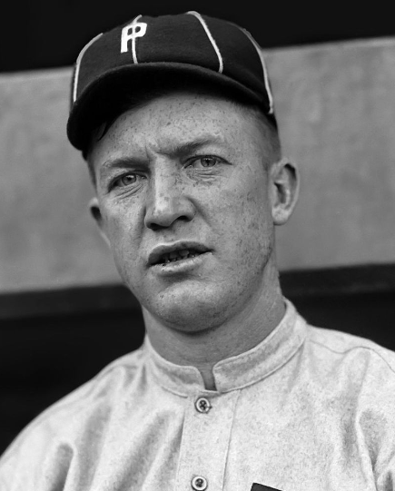 A black and white photograph of a baseball player wearing a cap with a "P" on it and a uniform. The player has a serious expression and a clean-shaven face with freckles. The background is blurred, suggesting it may be taken in a dugout or similar setting.