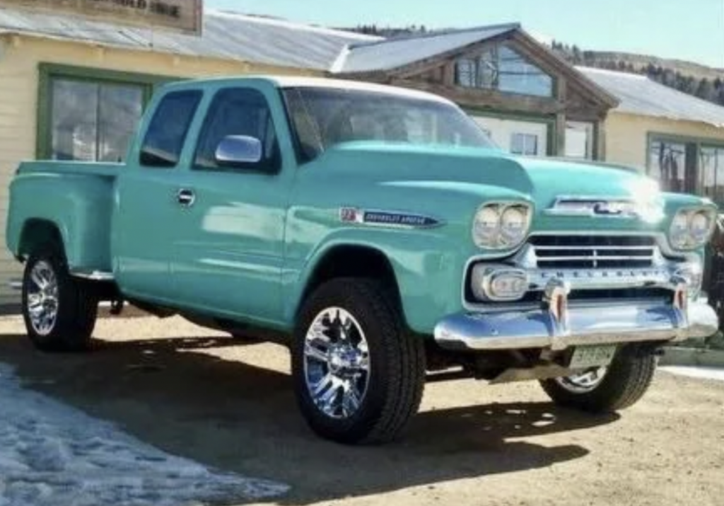 A mint green vintage Chevrolet Apache pickup truck with chrome wheels is parked in front of a building. Snow is partially visible on the ground. The truck has a classic design with rounded fenders and a prominent front grille.