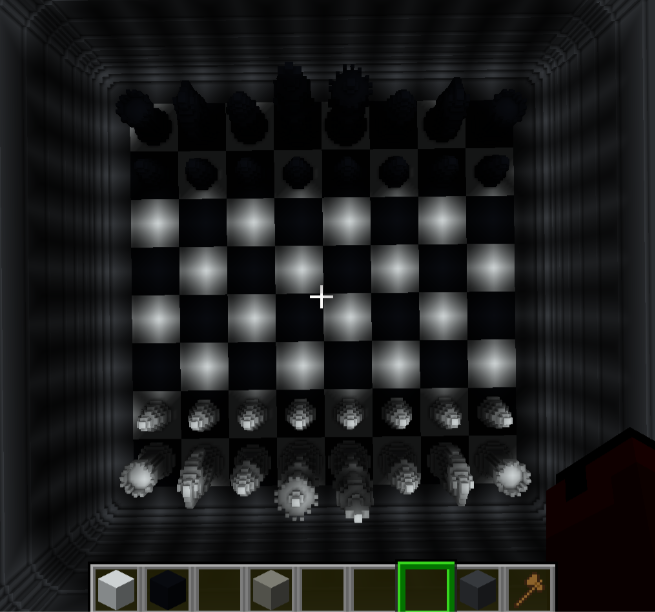 A top-down view of a chessboard in the game Minecraft, set inside a dimly lit, enclosed area. The board has alternating black and white squares with detailed chess pieces on each side. Below the board, a toolbar displays various blocks and a tool.