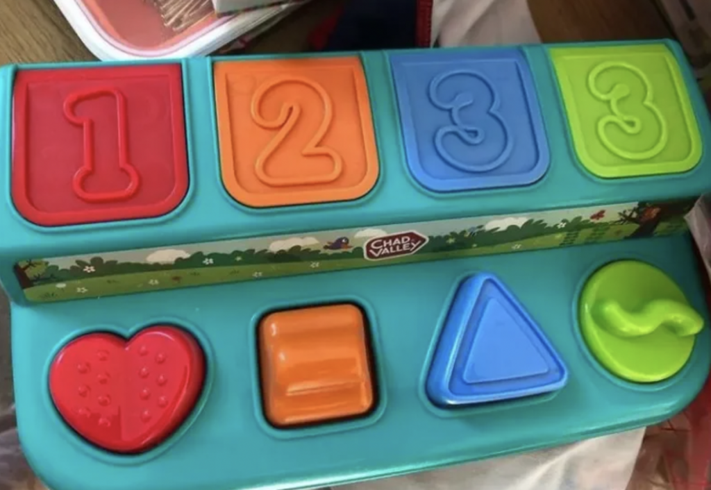 A children's shape and number sorter toy by Chad Valley. The toy features three pop-up panels with the numbers 1, 2, and 3 in red, orange, and blue, respectively. Below them are four shapes: a pink heart, an orange square, a blue triangle, and a green swirl.