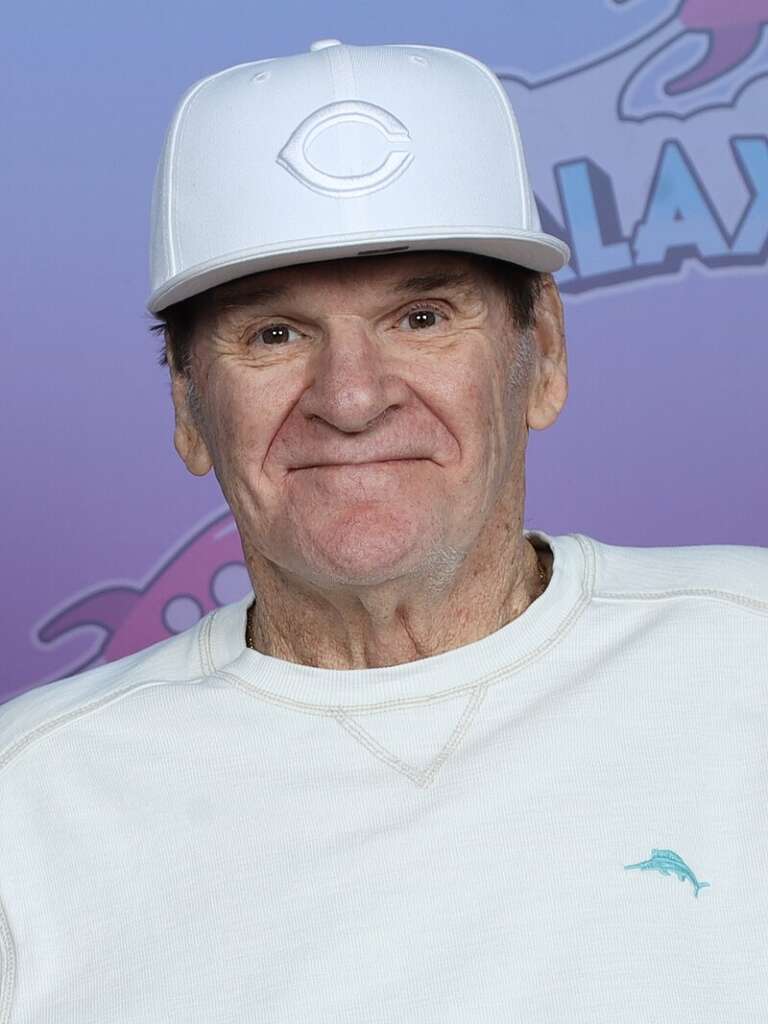 An older man wearing a white baseball cap and white long-sleeved shirt smiles against a colorful background. The hat features a stylized letter "C." He has a gentle expression and the backdrop includes partially visible playful graphics and text.