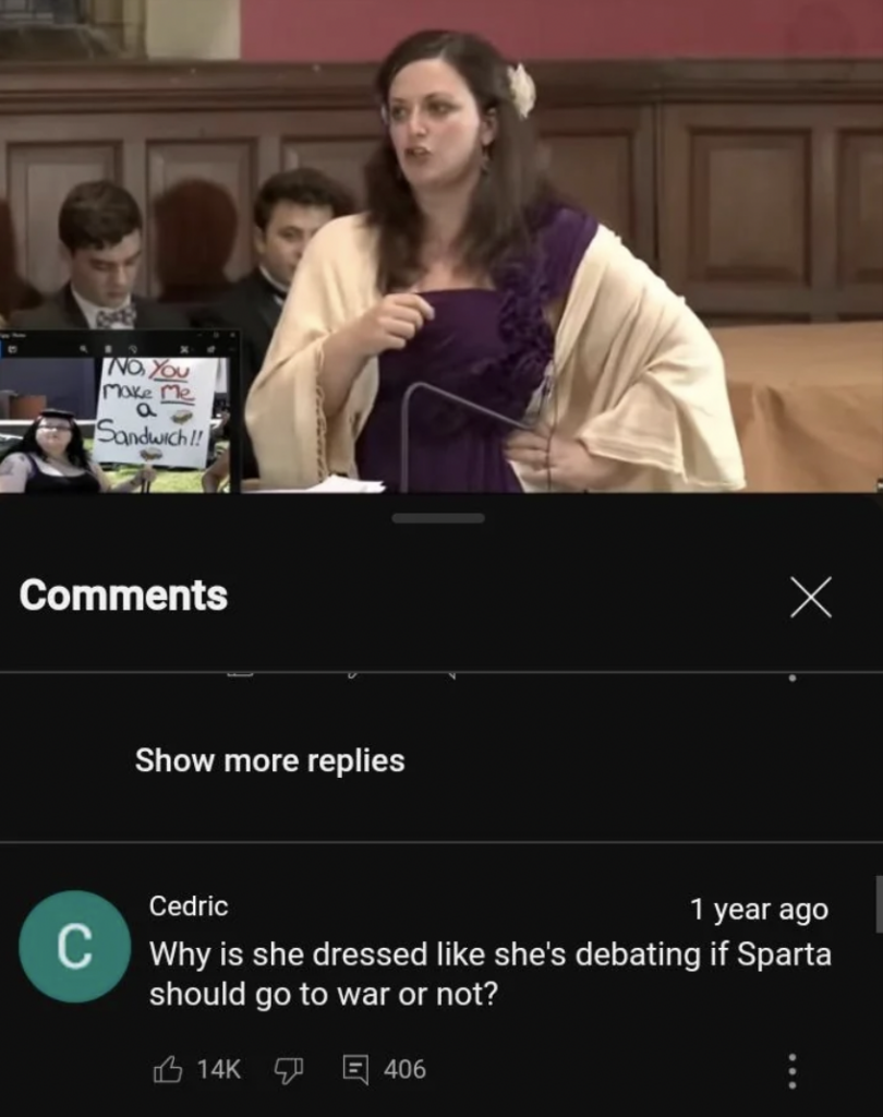 A woman in a toga-like dress, standing at a podium during a debate or speech, is speaking passionately. A comment below asks, "Why is she dressed like she's debating if Sparta should go to war or not?" with significant likes and replies.