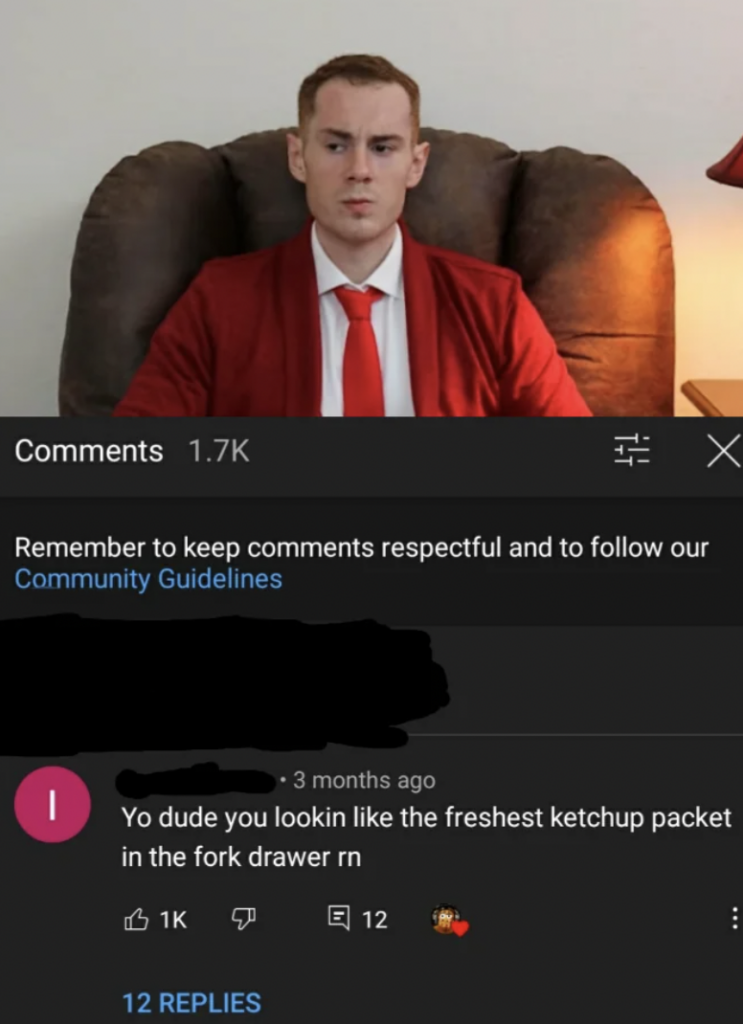 A man wearing a red suit and tie sits on a couch with a serious expression. Below the image is a YouTube comment section reading, "Yo dude you lookin like the freshest ketchup packet in the fork drawer rn" with 1K likes and 12 dislikes, plus 12 replies.