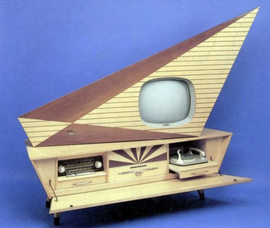 A vintage television set with an asymmetrical, angular wooden casing and a small screen on the right side. The lower section includes a built-in radio, storage compartments, and a turntable. The background is plain blue.