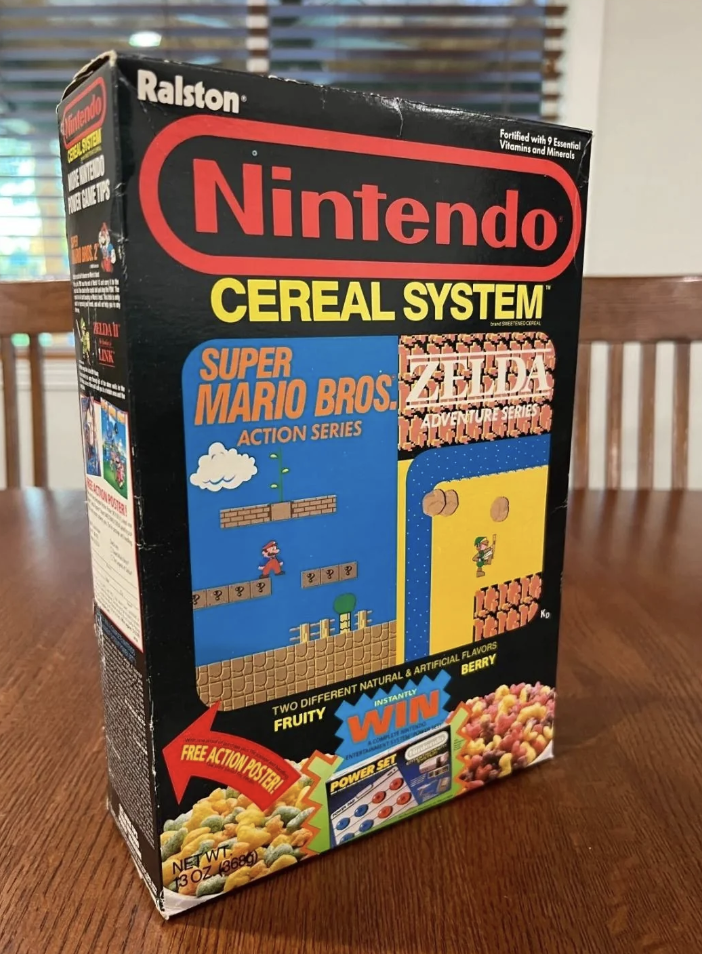 A photo of a vintage "Nintendo Cereal System" box featuring Super Mario Bros. and Zelda Adventure Series designs. The box is predominantly black with colorful graphics, highlighting images of Mario jumping and Link from Zelda. It sits on a wooden table.